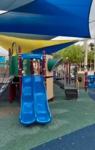 Accessible playground area with slides, ramps, and climbing structures at Morgan’s Wonderland, shaded with a blue canopy.